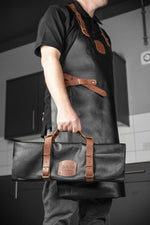 Chef holding Global leather knife roll case for kitchen knife storage wearing matching Global chef's apron