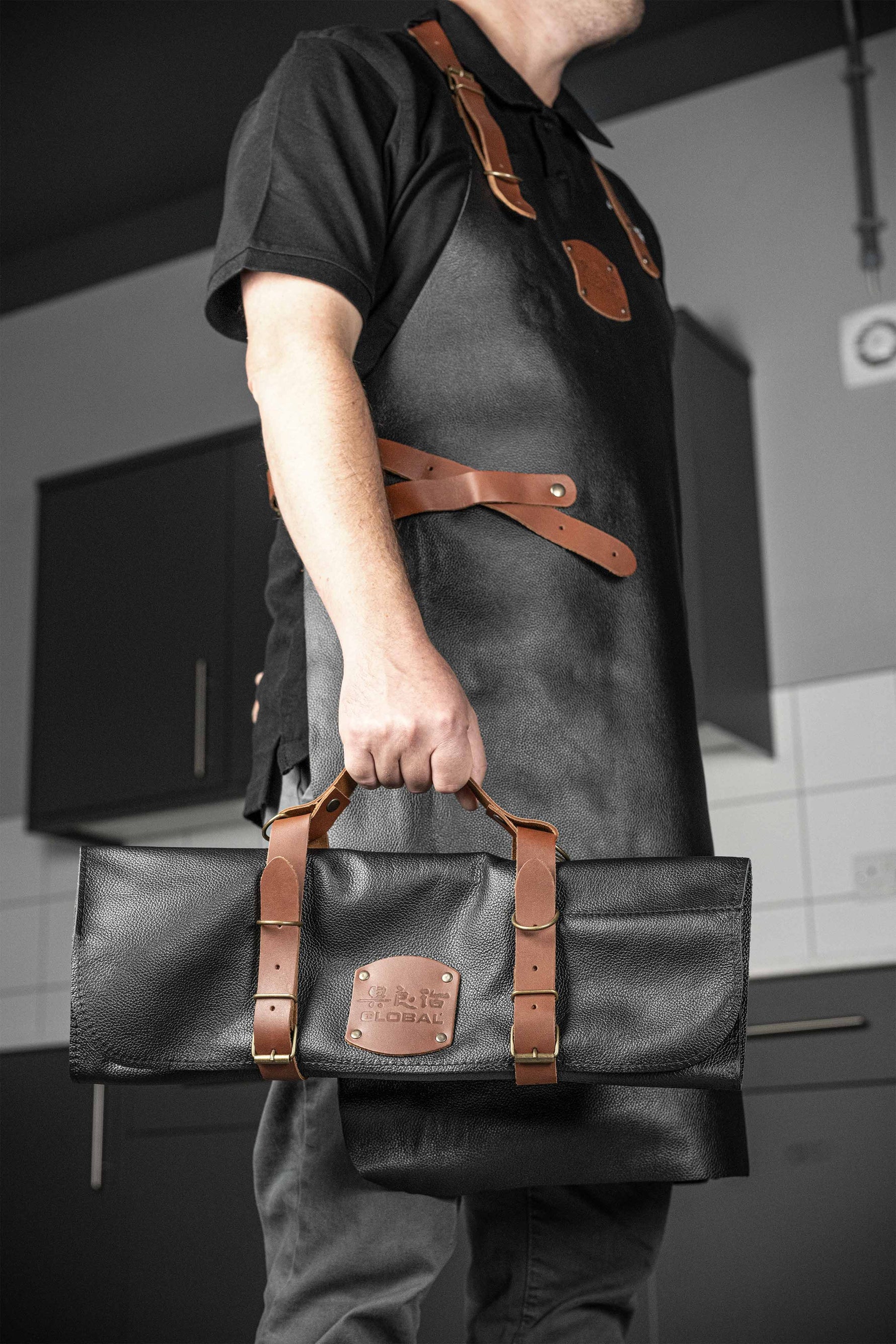 Chef holding Global leather knife roll case for kitchen knife storage wearing matching Global chef's apron