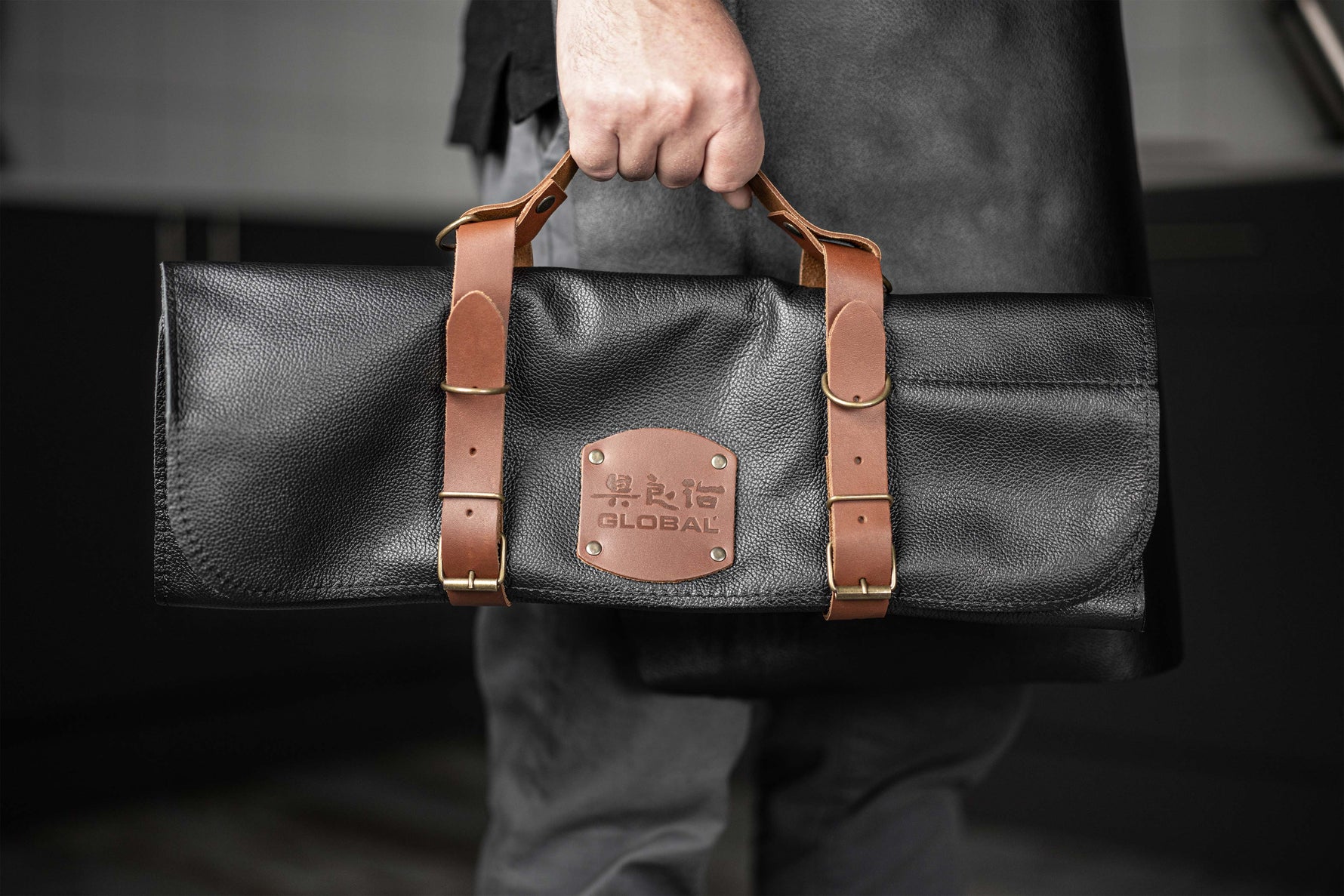 Cook holding Global leather knife bag for compact kitchen knife storage with matching genuine leather apron for cooking, bbqs and grilling.