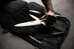 Chef holding Global G-2 chef's knife next to black leather knife roll case with 5 slots