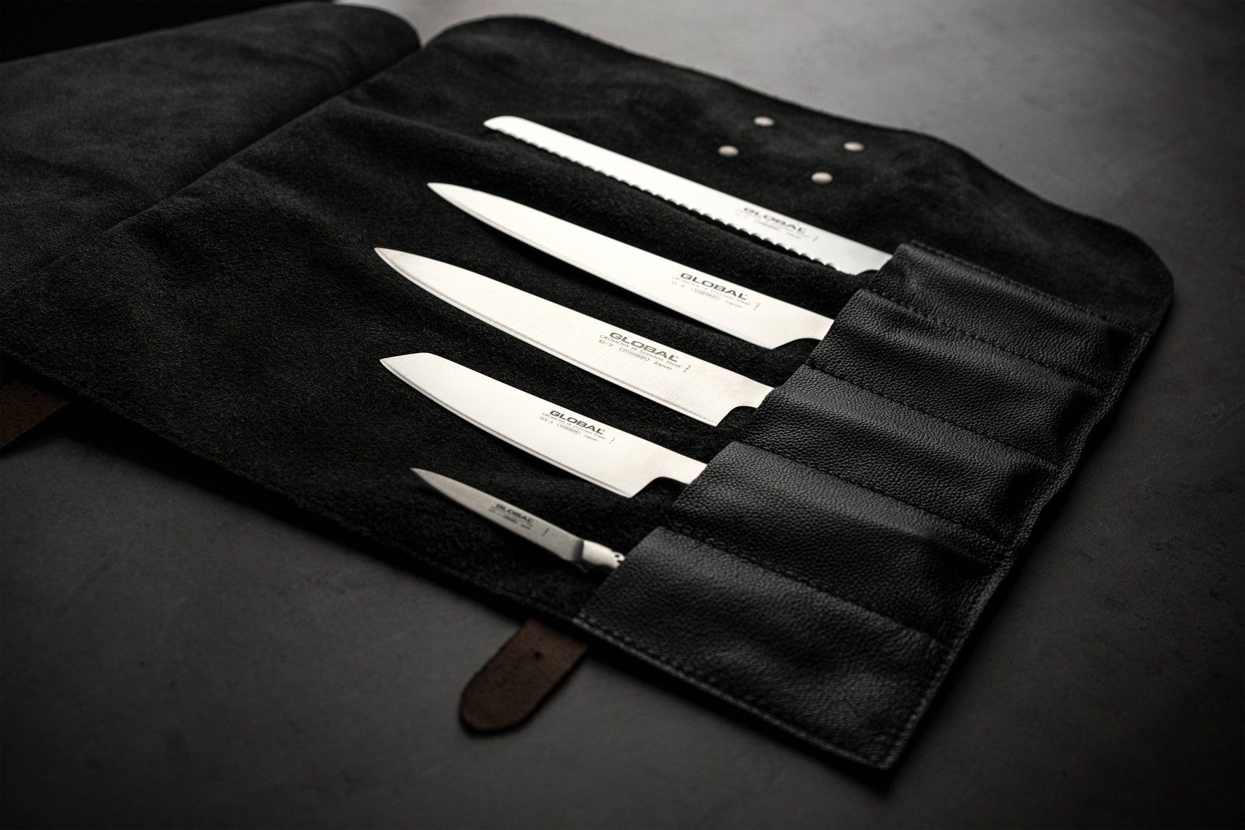 Open black leather knife roll case with 5 slots holding Global Japanese chef knives set