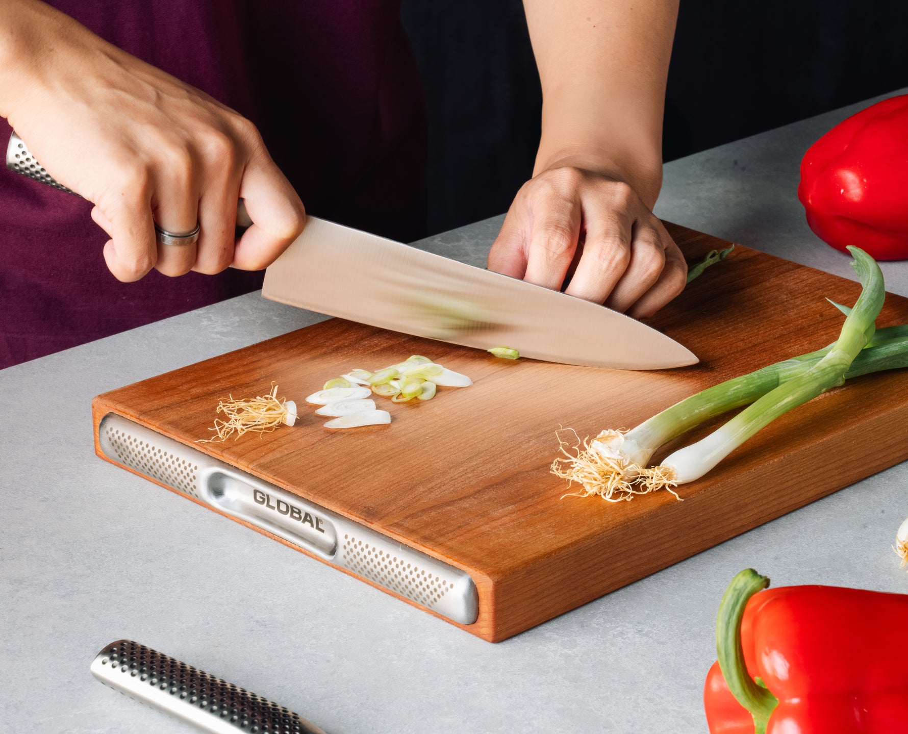 Home cook cutting spring onions and red pepper on Global premium kitchen cutting board made of solid cherry wood.