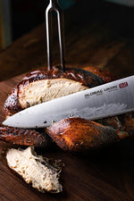 Global carving fork in sliced smoked chicken with a Global Ukon knife on a wooden surface