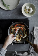 Foodie chef using GLOBAL professional kitchen tweezers for fine control and precision to prepare seafood in a frying pan in a home kitchen.