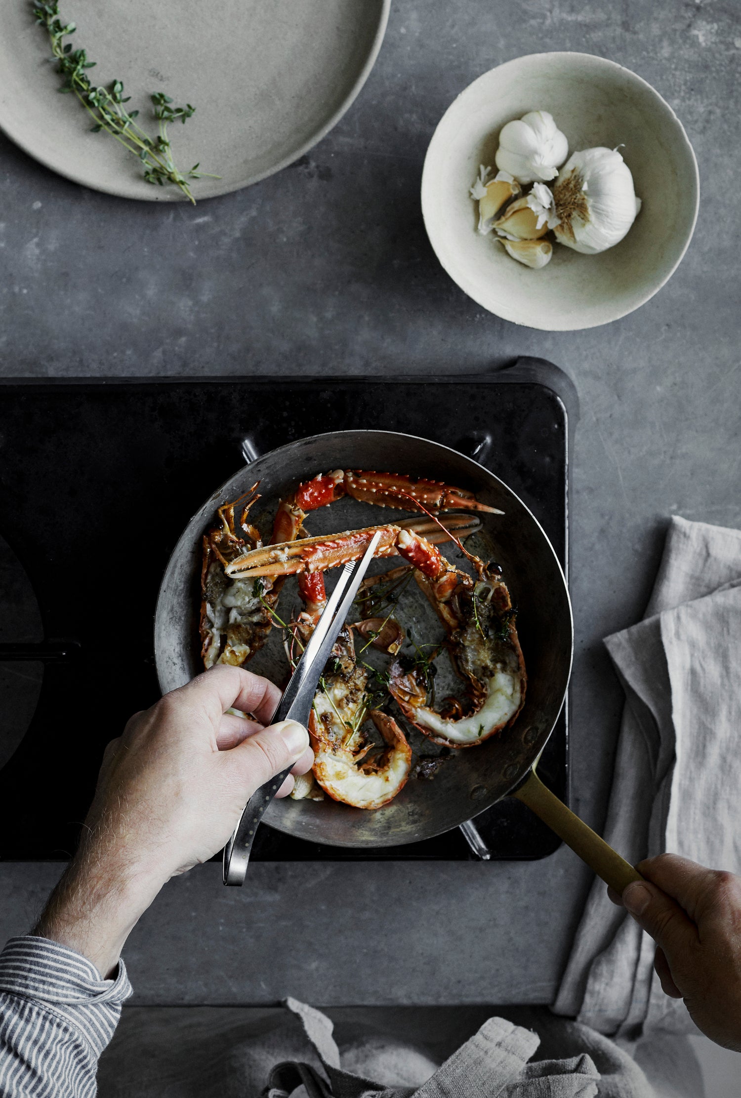 Foodie chef using GLOBAL professional kitchen tweezers for fine control and precision to prepare seafood in a frying pan in a home kitchen.