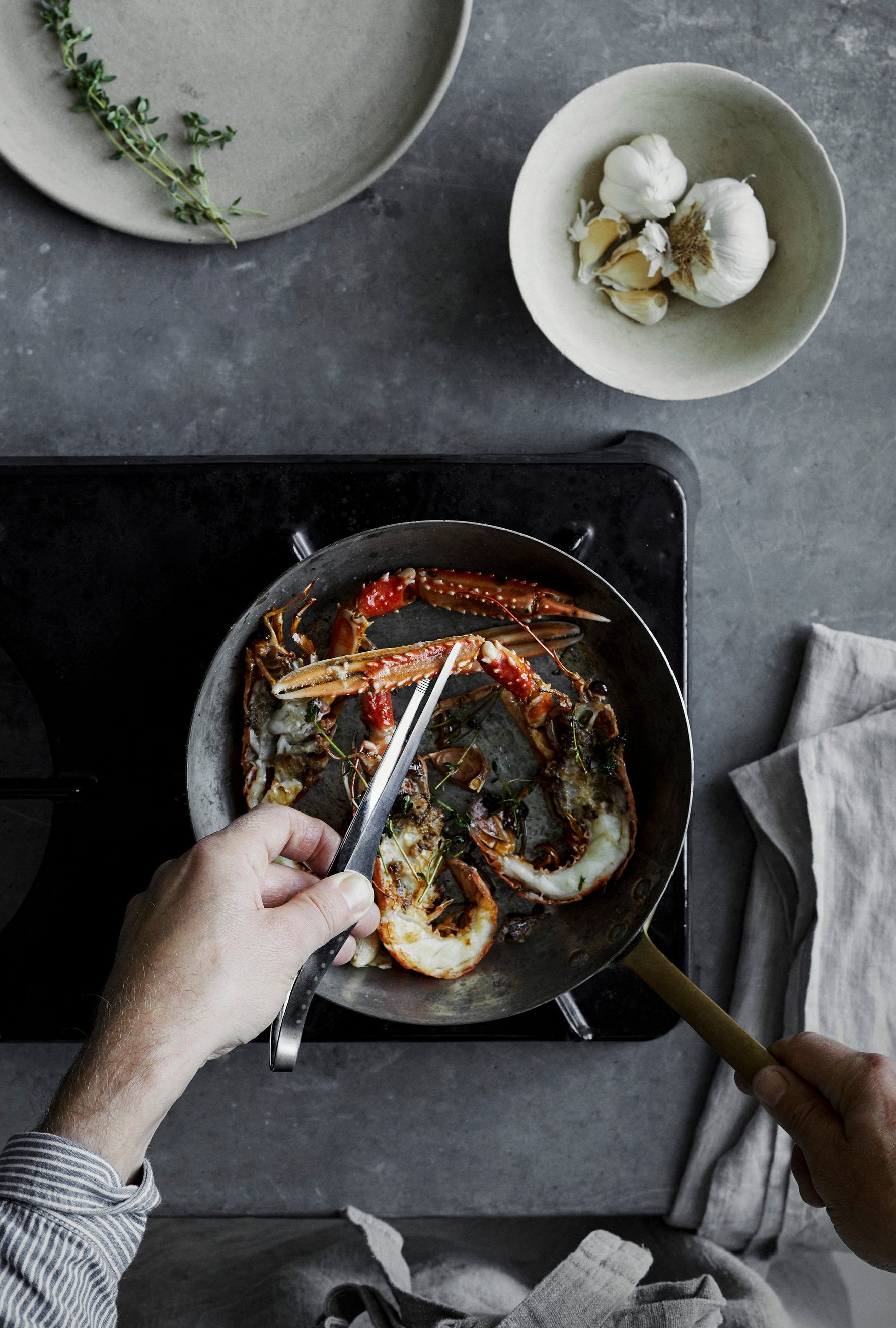 Foodie chef using GLOBAL professional kitchen tweezers for fine control and precision to prepare seafood in a frying pan in a home kitchen.