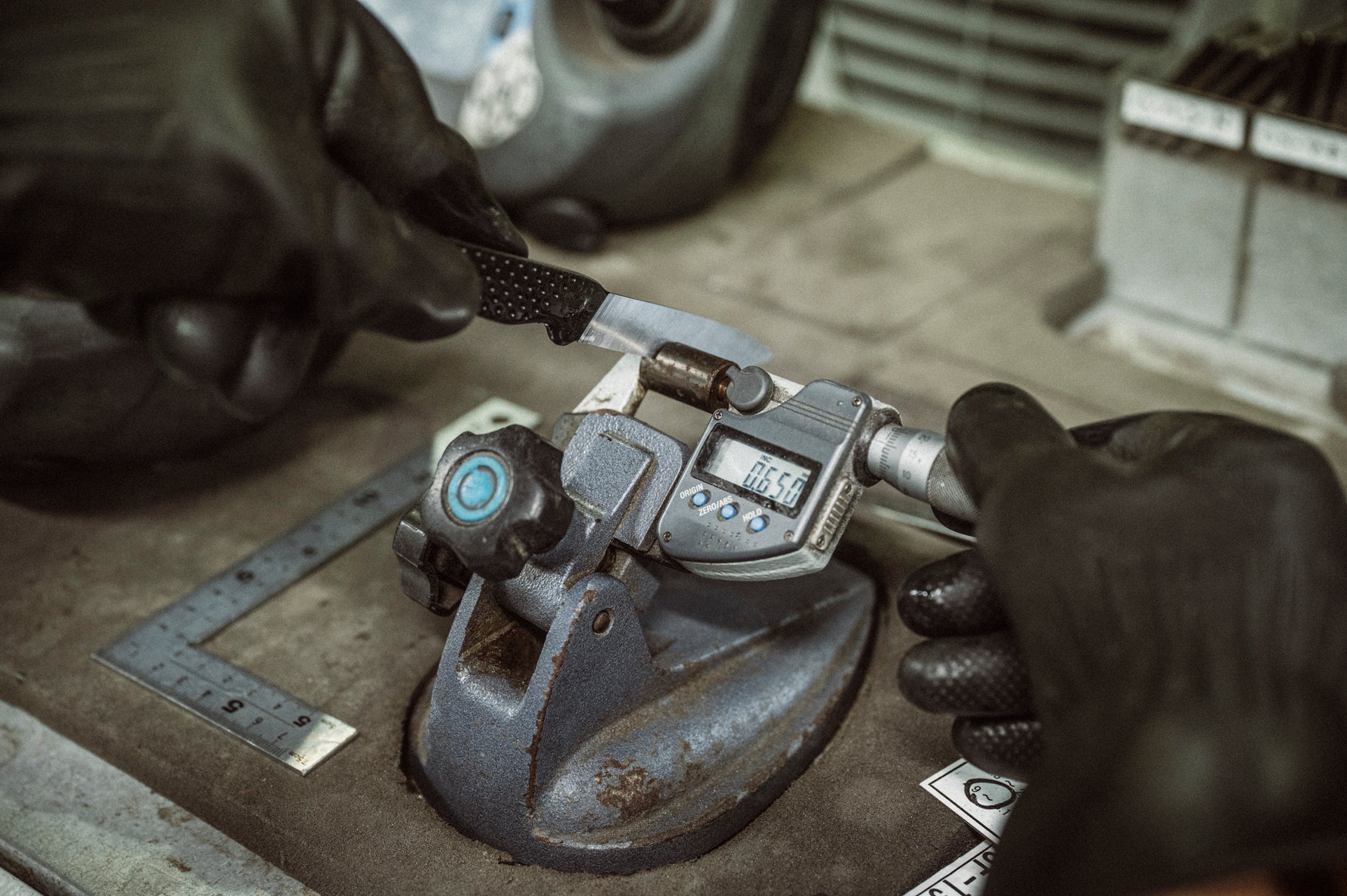 Close-up of a measurement tool with small Global knife with hands wearing gloves on a workshop surface.