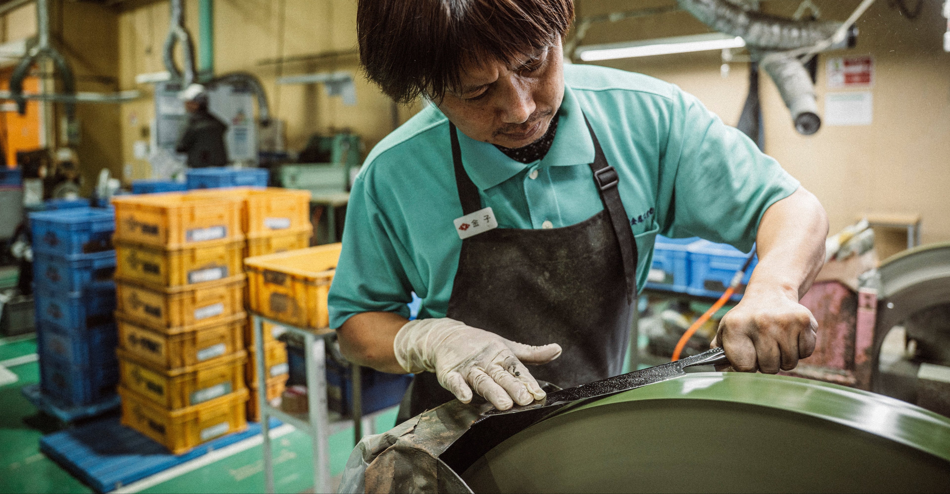 Person working in Global Yoshikin factory setting with equipment and crates in the background