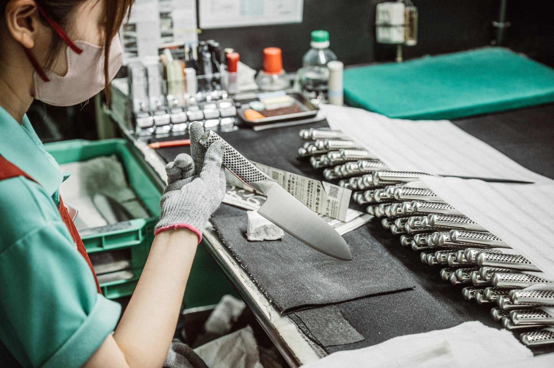 Person working on a manufacturing line in Yoshikin factory, Japan, checking the quality and sharpness of Global knives.